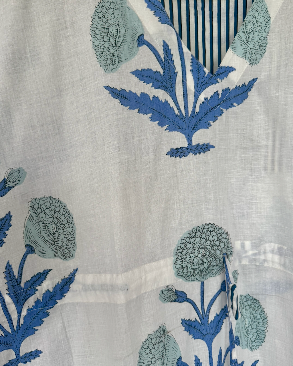 White cotton fabric with blue and light blue floral block print embroidery, featuring a striped collar detail.